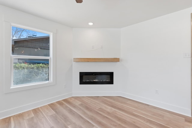 unfurnished living room with baseboards, a glass covered fireplace, light wood-style flooring, and a healthy amount of sunlight