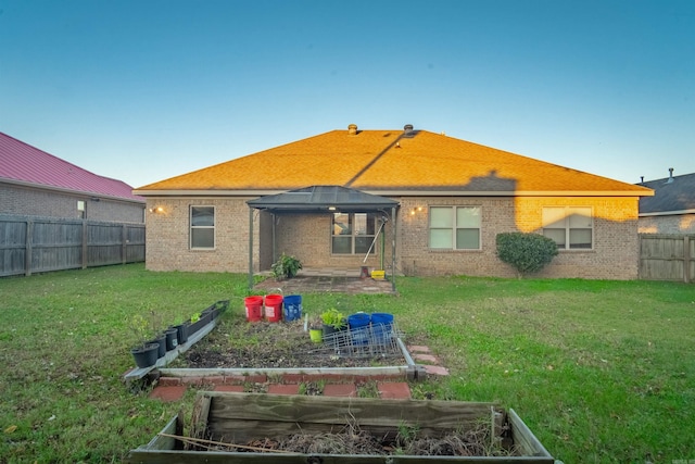 rear view of house with a gazebo, brick siding, a lawn, and a vegetable garden