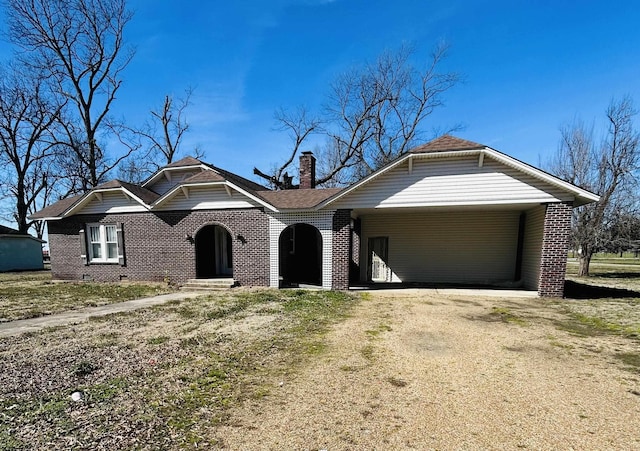 view of front facade featuring driveway, brick siding, a chimney, and crawl space