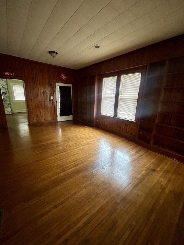 unfurnished living room with wood walls, wood finished floors, and visible vents