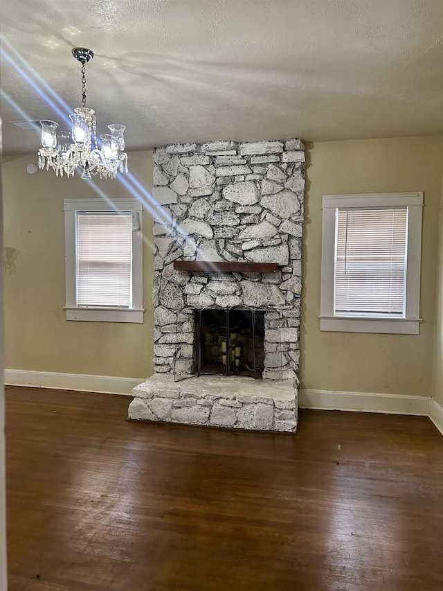 unfurnished living room with a textured ceiling, a stone fireplace, wood finished floors, baseboards, and an inviting chandelier