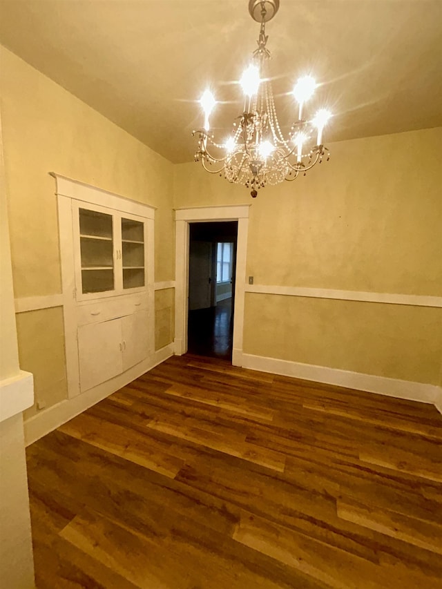 spare room with baseboards, dark wood-style flooring, and an inviting chandelier