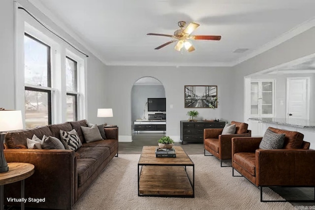 living area featuring a ceiling fan, baseboards, arched walkways, and crown molding