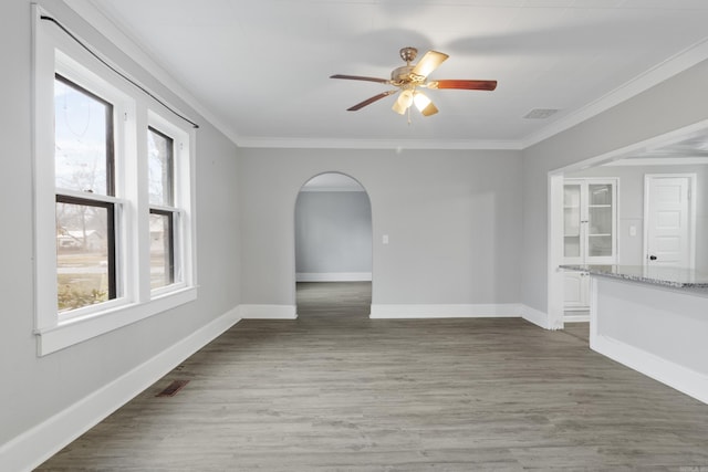 spare room with arched walkways, visible vents, ornamental molding, wood finished floors, and baseboards