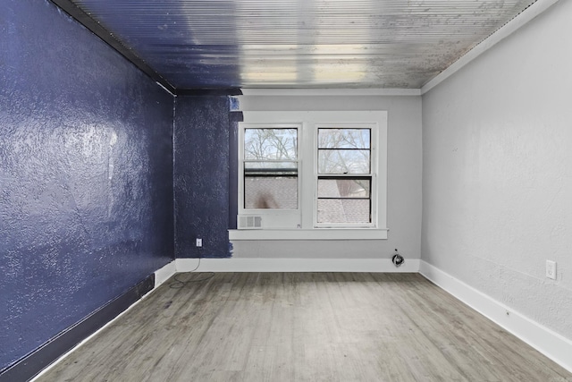 unfurnished room featuring baseboards, wood finished floors, and a textured wall