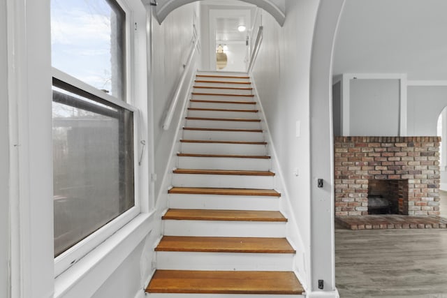 staircase with arched walkways, a fireplace, and wood finished floors