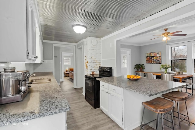 kitchen with electric range, white cabinets, a breakfast bar, light wood-type flooring, and a sink