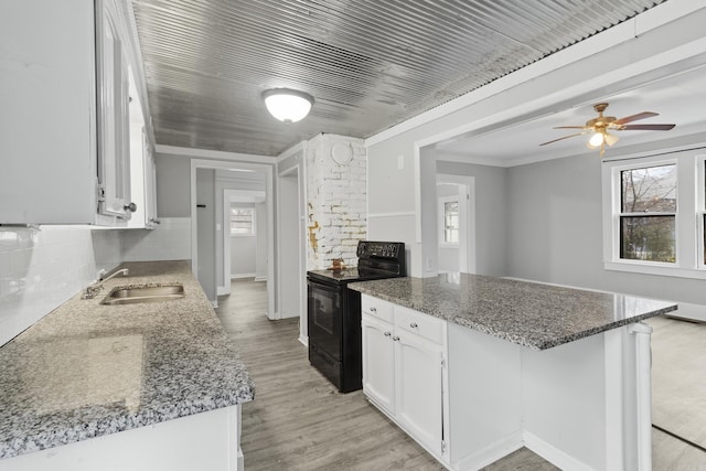 kitchen featuring black / electric stove, a peninsula, a sink, white cabinets, and dark stone counters