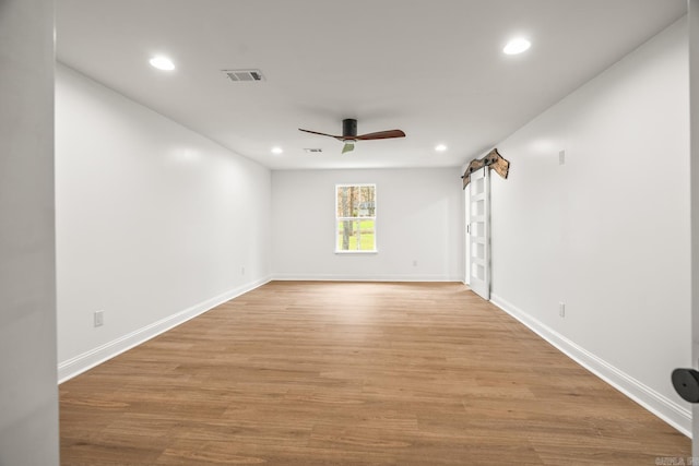 empty room with light wood finished floors, a barn door, visible vents, ceiling fan, and recessed lighting