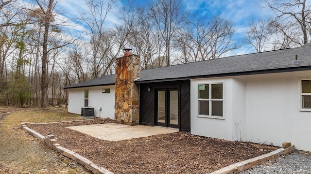 back of house with roof with shingles, a chimney, central AC, and a patio