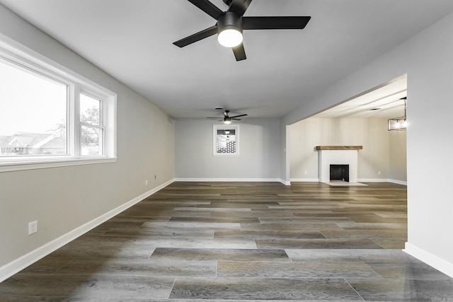 unfurnished living room featuring a fireplace with flush hearth, a ceiling fan, baseboards, and wood finished floors