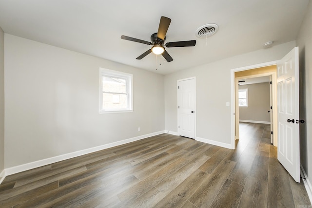 unfurnished bedroom with dark wood-style floors, multiple windows, visible vents, and baseboards