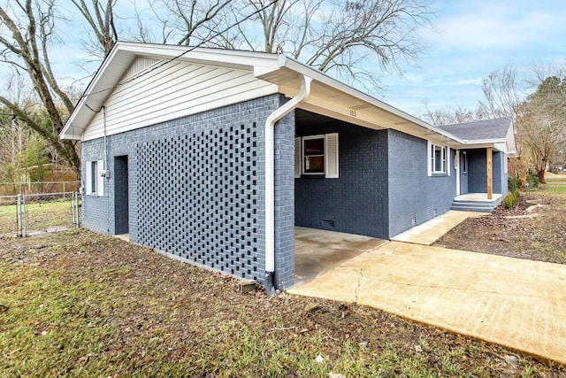 view of side of home with brick siding, crawl space, a gate, fence, and driveway