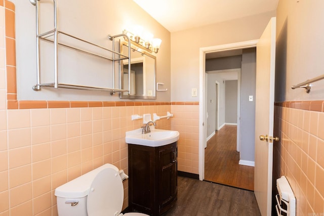 half bath with a wainscoted wall, toilet, wood finished floors, and tile walls