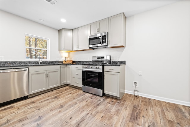 kitchen with light wood-style flooring, recessed lighting, stainless steel appliances, a sink, and baseboards