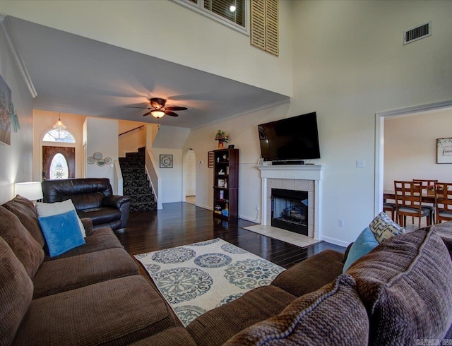 living room with visible vents, a ceiling fan, a tiled fireplace, stairway, and wood finished floors