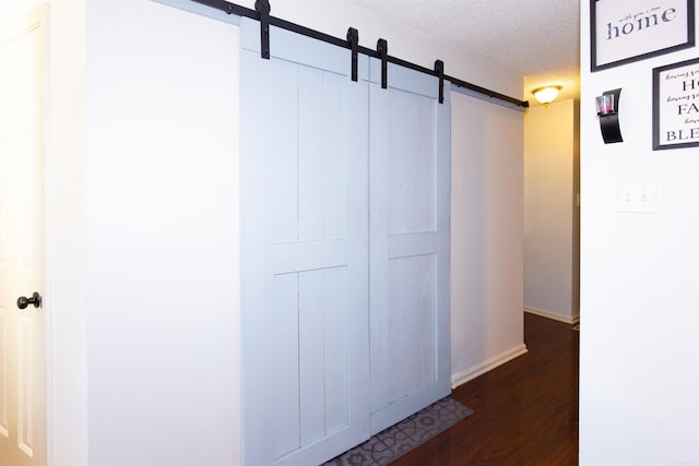 corridor with wood finished floors, a textured ceiling, baseboards, and a barn door