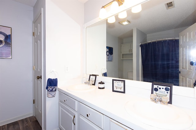 bathroom with wood finished floors, visible vents, a sink, and double vanity