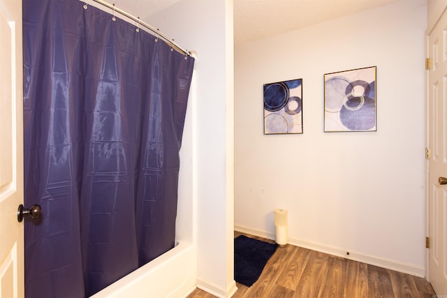 bathroom featuring a textured ceiling, baseboards, wood finished floors, and shower / tub combo with curtain