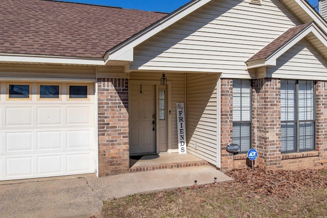 property entrance featuring a shingled roof, brick siding, and a garage