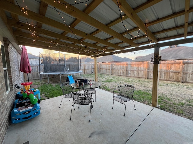 view of patio with outdoor dining space, a trampoline, and a fenced backyard