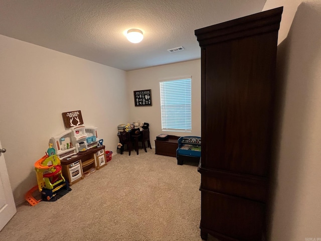 recreation room featuring a textured ceiling, carpet floors, and visible vents