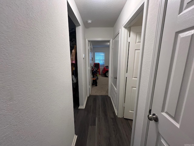 hallway with dark wood-type flooring, a textured wall, and a textured ceiling