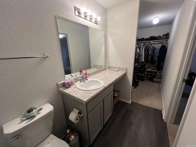 bathroom featuring a textured wall, toilet, wood finished floors, vanity, and a walk in closet