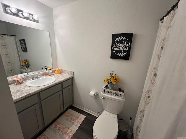 bathroom with toilet, wood finished floors, vanity, and baseboards