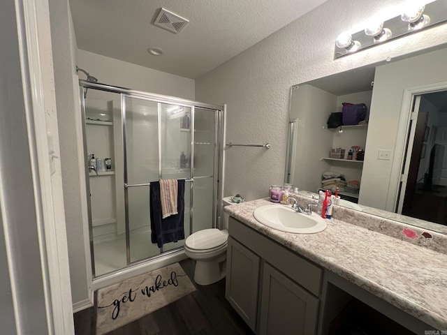 full bath featuring a textured wall, toilet, vanity, visible vents, and a stall shower