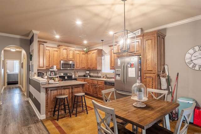 kitchen with arched walkways, appliances with stainless steel finishes, light wood-style floors, a sink, and a kitchen breakfast bar