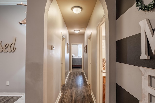 hallway with arched walkways, dark wood-style flooring, and baseboards