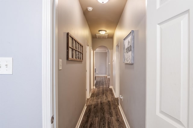 hall featuring baseboards, arched walkways, and dark wood-type flooring