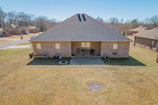 back of property featuring a patio, a yard, roof with shingles, and brick siding