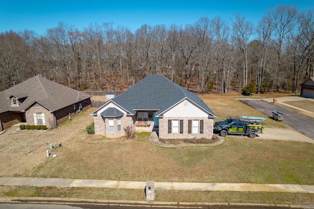 view of front of home featuring stone siding, roof with shingles, and a front yard