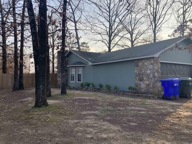 view of home's exterior featuring a garage, stone siding, and fence