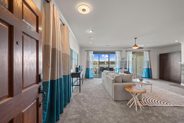 living room featuring ceiling fan, ornamental molding, baseboards, and light colored carpet