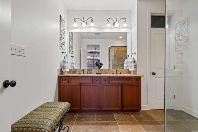 bathroom with a tile shower, double vanity, a sink, and visible vents