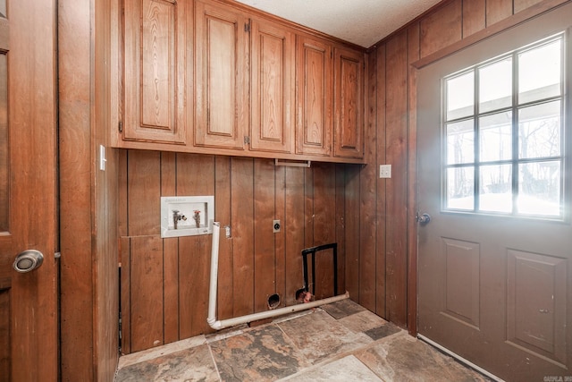 clothes washing area with hookup for a washing machine, stone finish floor, cabinet space, and wood walls