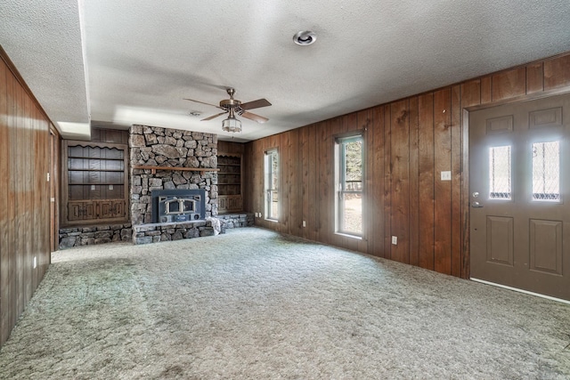 unfurnished living room featuring carpet floors, a fireplace, a ceiling fan, wood walls, and a textured ceiling