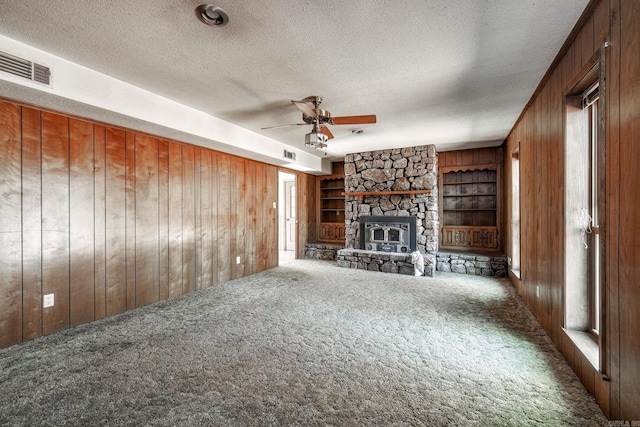 unfurnished living room with a textured ceiling, built in shelves, carpet floors, wood walls, and visible vents