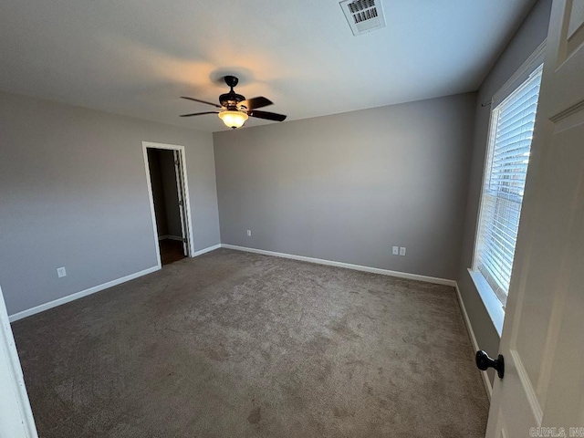 spare room with baseboards, visible vents, dark colored carpet, and a ceiling fan