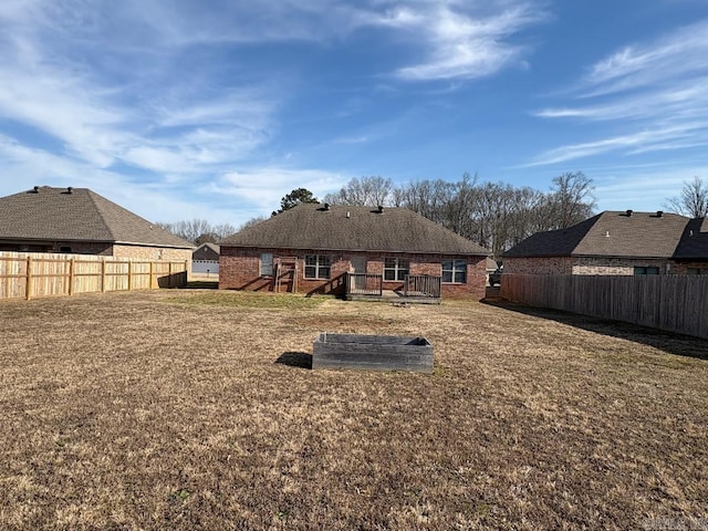 rear view of house with a deck, a yard, brick siding, and a fenced backyard