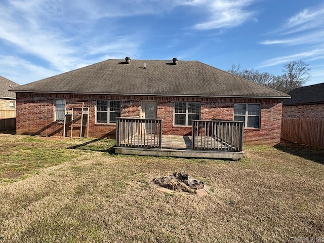 back of property featuring brick siding, fence, roof with shingles, a lawn, and a wooden deck