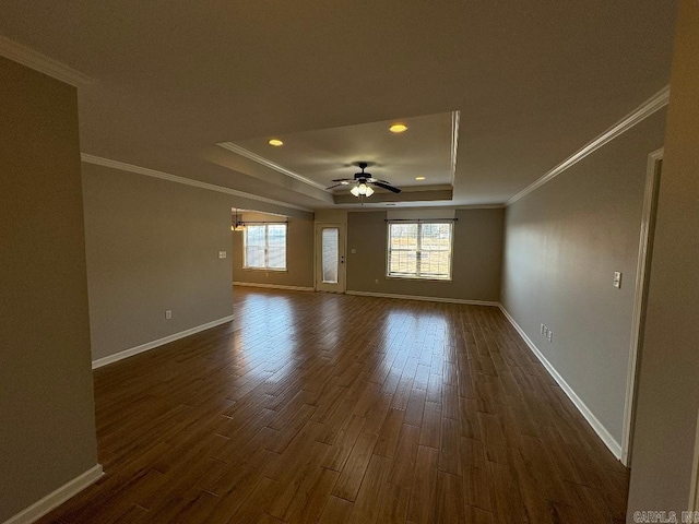 unfurnished room featuring dark wood-type flooring, a ceiling fan, baseboards, ornamental molding, and a raised ceiling