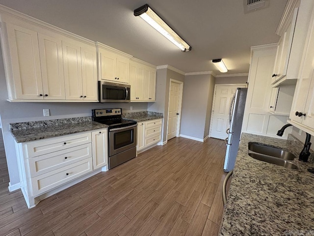 kitchen featuring dark wood-style floors, appliances with stainless steel finishes, ornamental molding, white cabinetry, and a sink