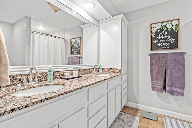 bathroom featuring double vanity, wood finished floors, a sink, and baseboards