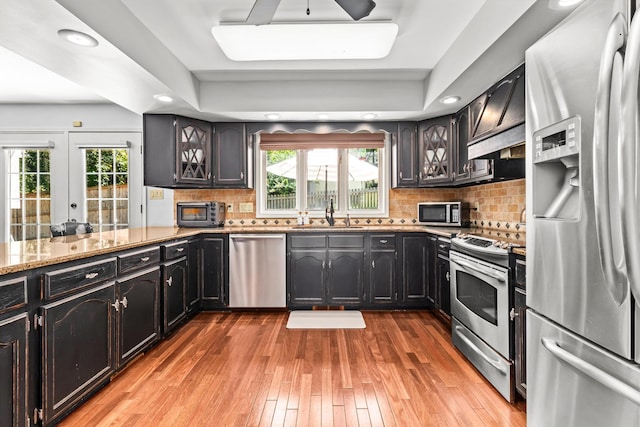 kitchen with custom exhaust hood, stainless steel appliances, backsplash, a sink, and light wood-type flooring