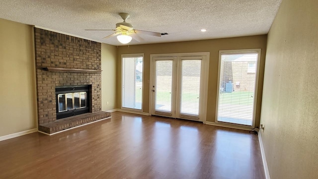 unfurnished living room with a textured ceiling, a fireplace, wood finished floors, a ceiling fan, and baseboards