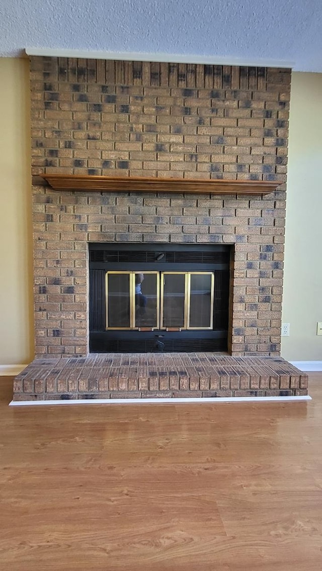 interior details featuring a textured ceiling, a brick fireplace, wood finished floors, and baseboards